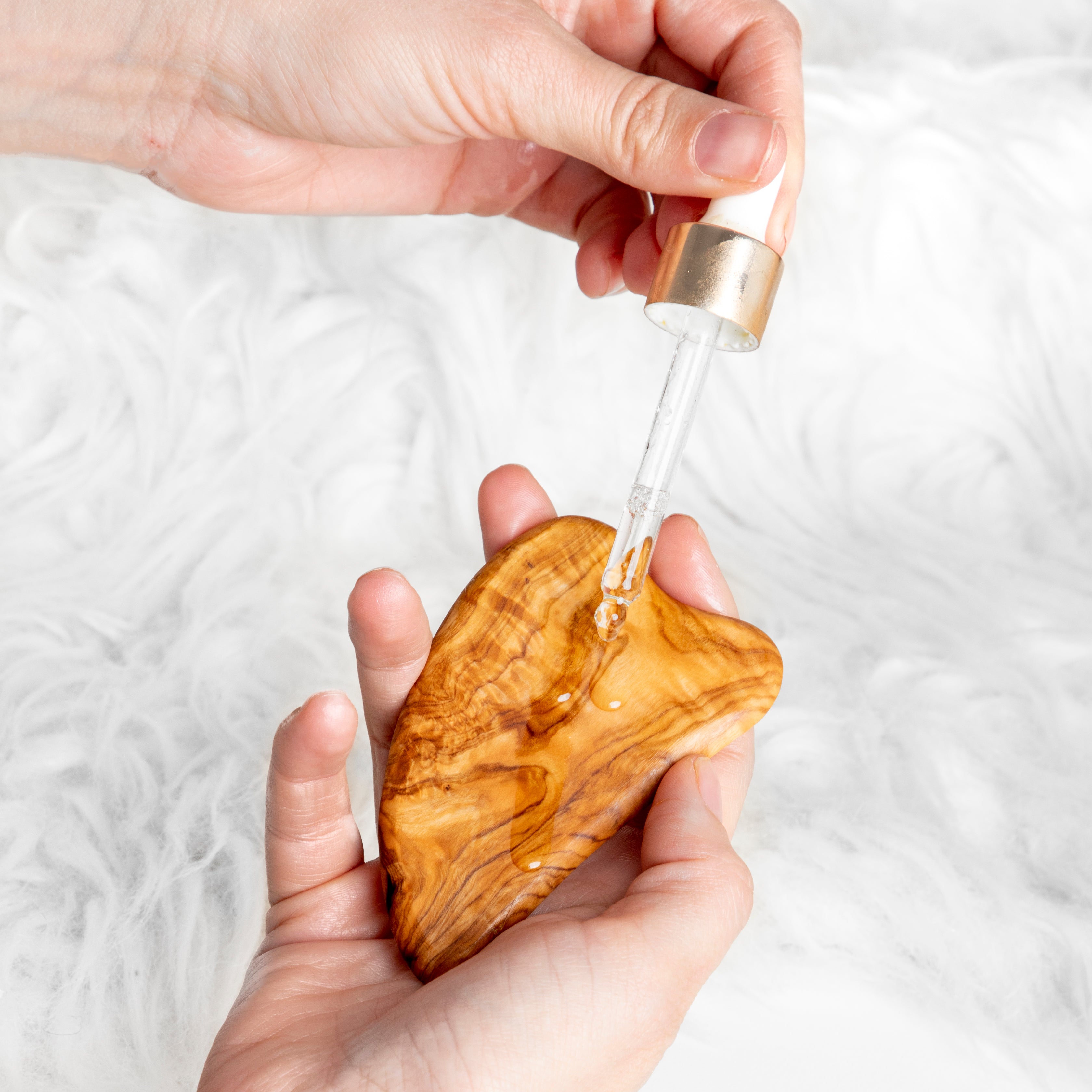 Facial oil dropper above olive wood gua sha, illustrating skincare massage routine.