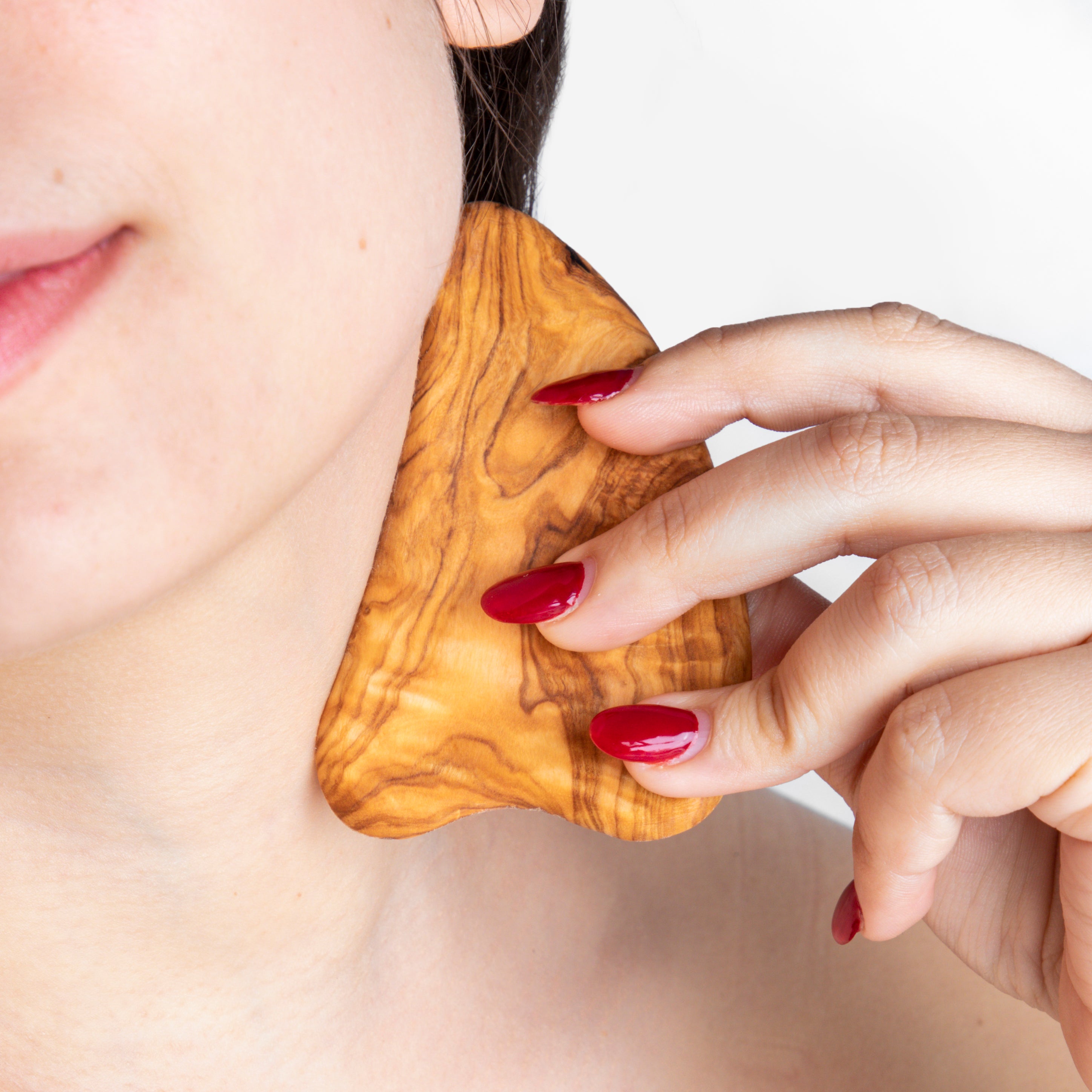 Model gliding olive wood gua sha along the cheek for lifting and de-puffing.