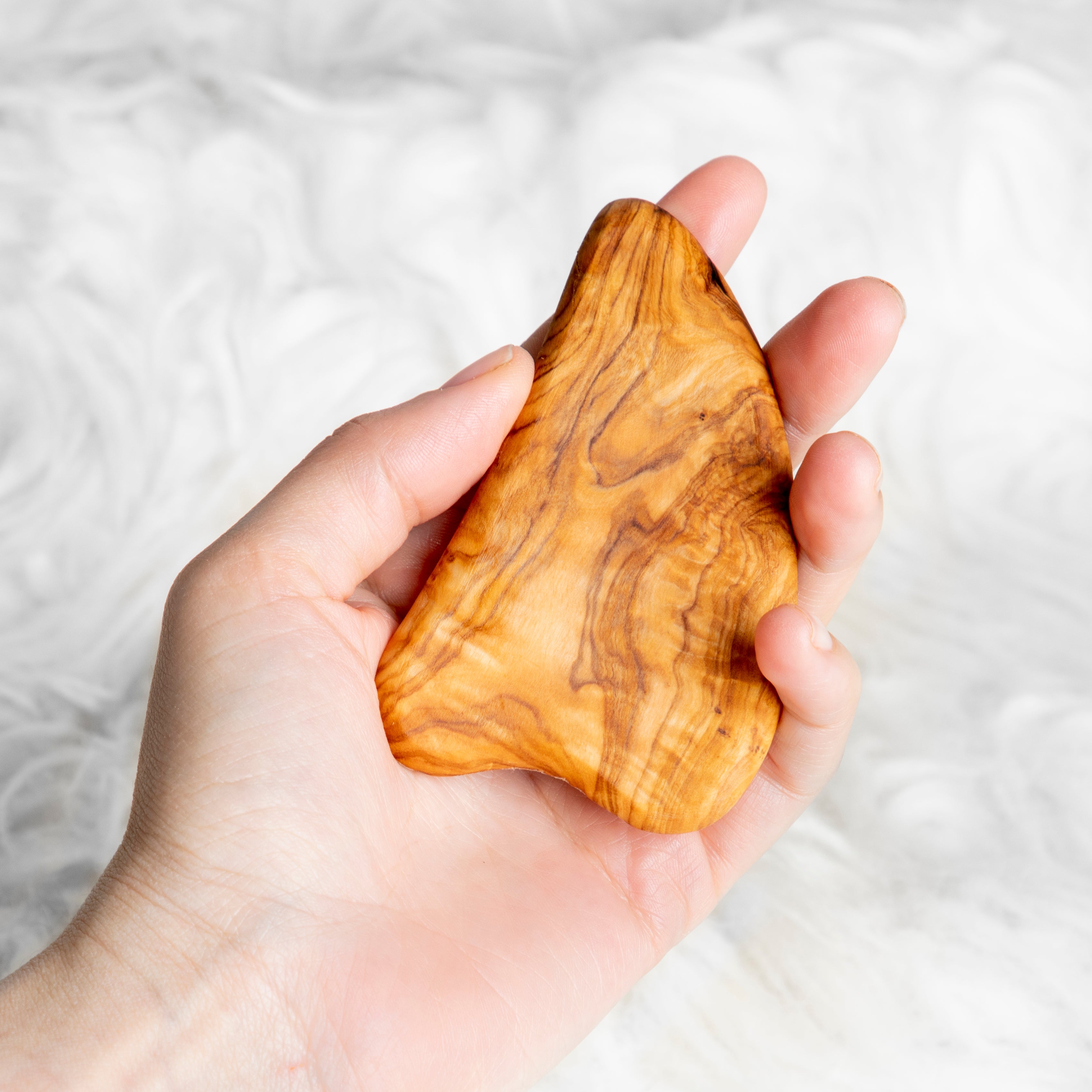 Olive wood gua sha resting in palm, showing size and natural grain pattern.