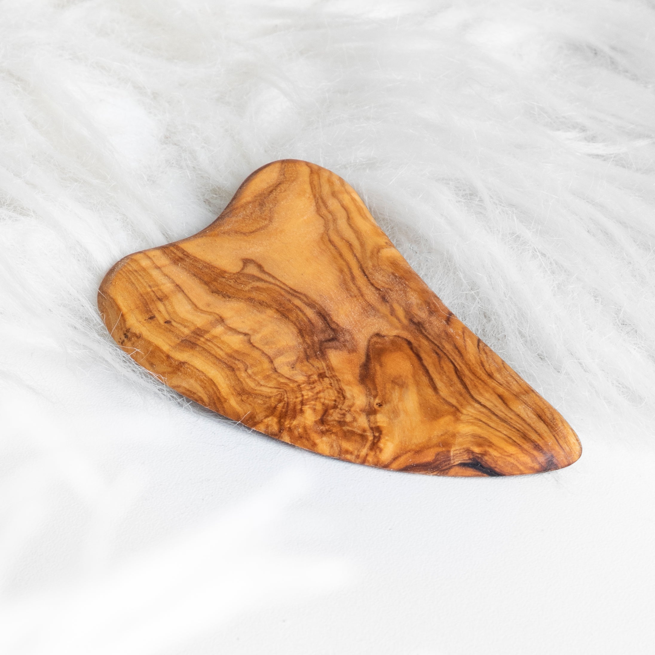 Olive wood gua sha facial massage tool, heart-shaped with smooth edges on white background.